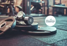 Amazing Benefits of Strength Training: Get Stronger, Live a Better A close-up of gym equipment featuring iron weight plates and two chrome dumbbells on a rubber gym floor.
